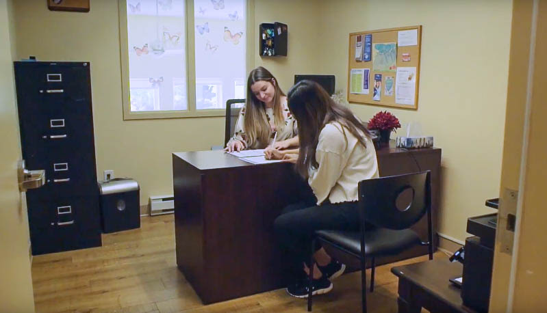 two women in an office space on either side of a desk looking at paper work