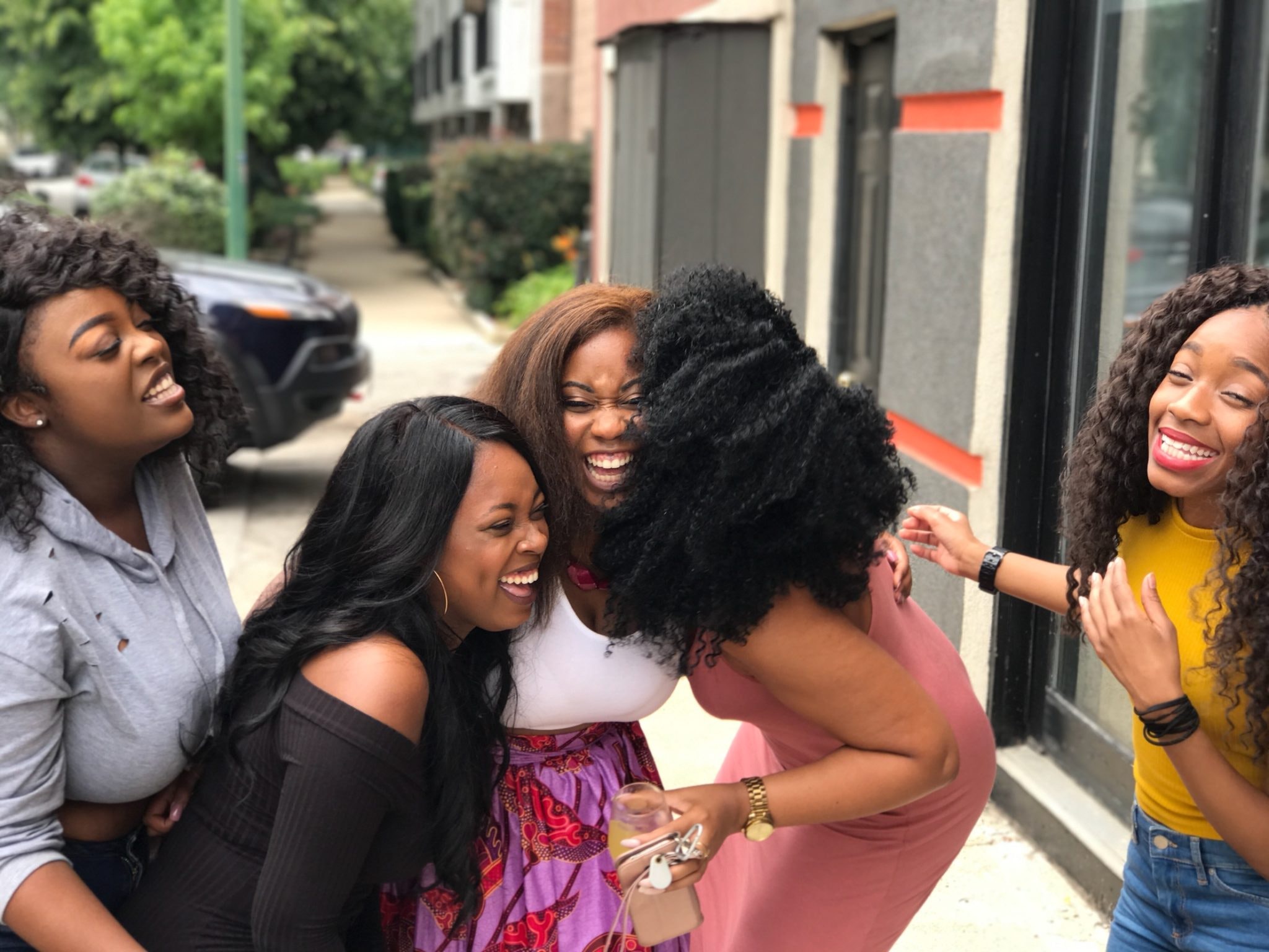 Group of five women, laughing together on a sidewalk.