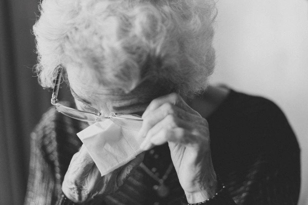 Black and white photo of an older woman wiping her eye with a tissue