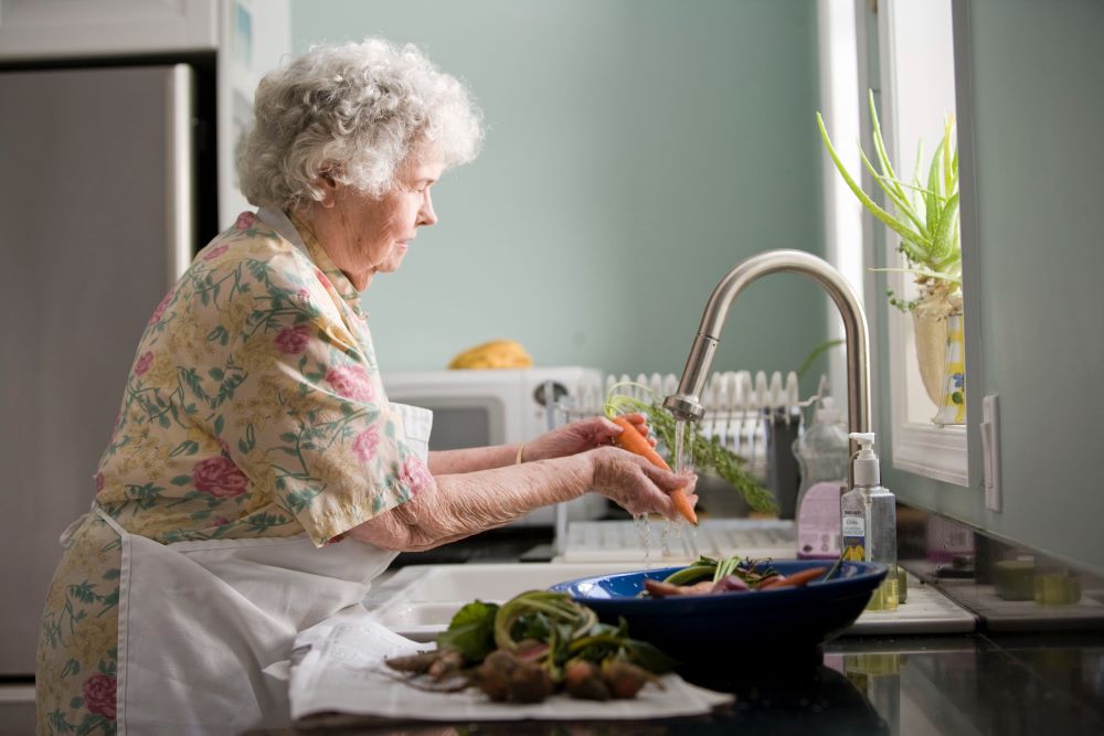 Older woman washing a carrot in her kitchen sink