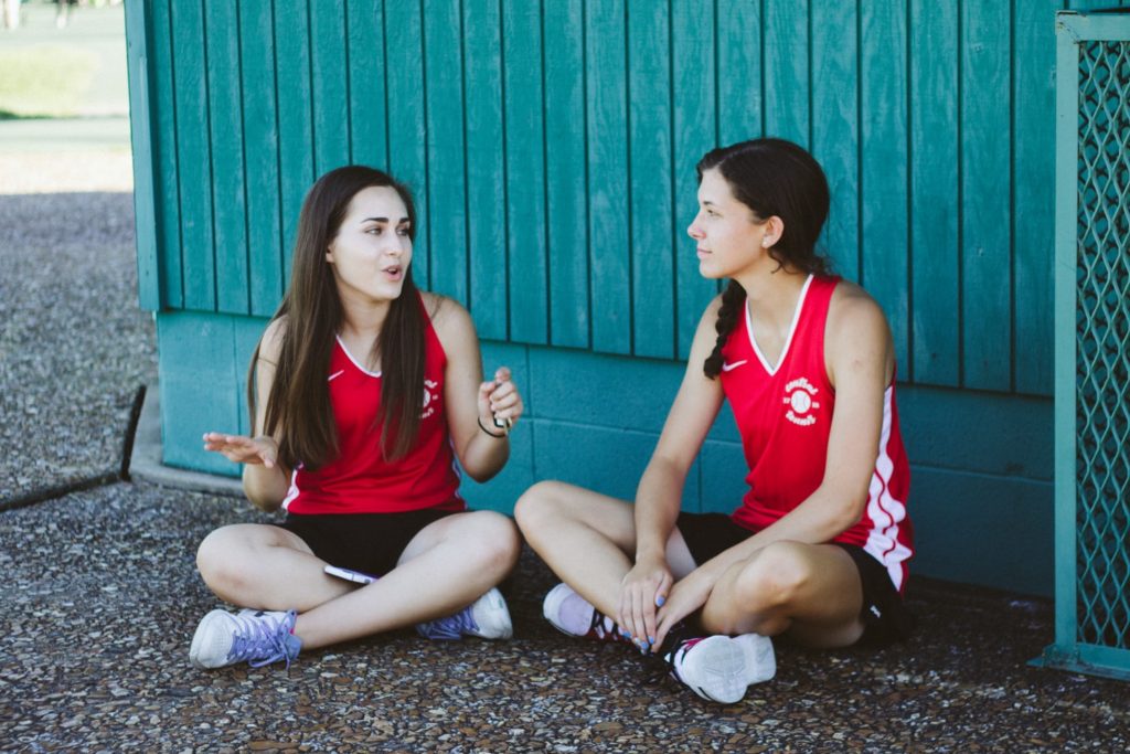 Two people sit on ground and talk to each other