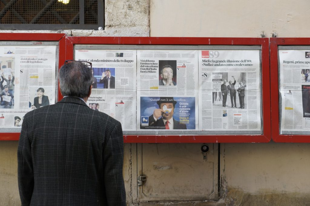 A man stands in front of a collection of newspapers