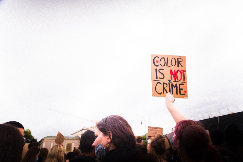 A group of protestors. One is holding up a sign reading "color is not a crime"