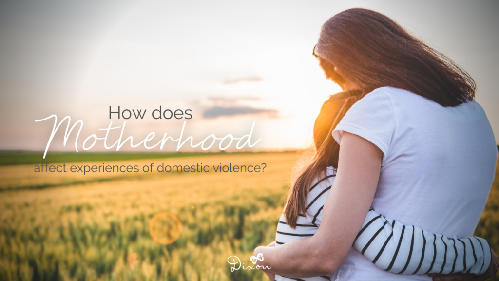 A mother and daughter hug in a field, backs facing the camera. Text floats beside them reading "How does motherhood affect experiences of domestic violence"