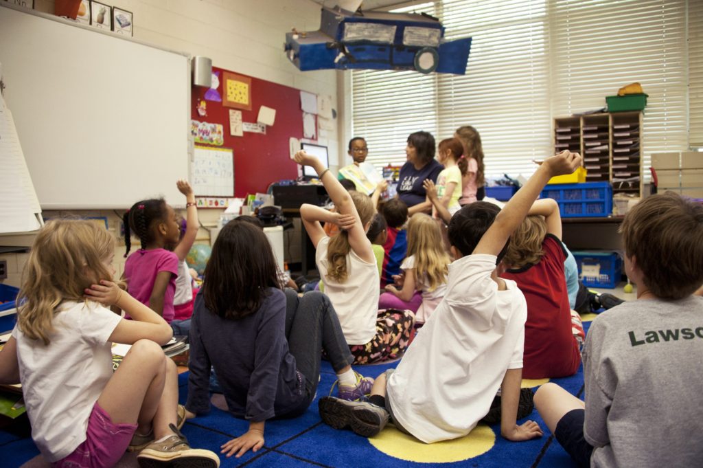 A group of children sit on the ground at daycare.